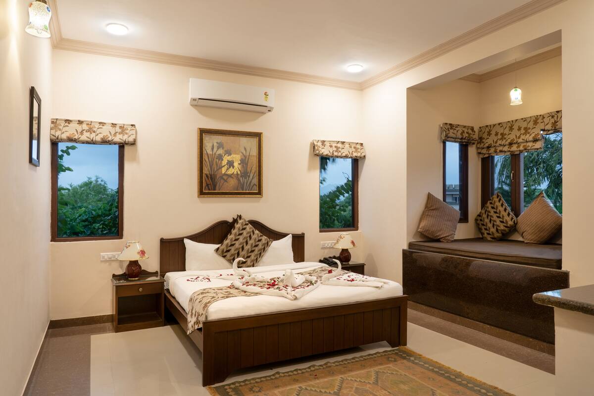 A bedroom with a bed, bedside tables, an air conditioner, a window with a view, and a built-in bench with cushions.