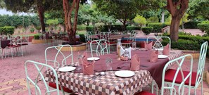 An outdoor dining area with checkered tablecloths, metal chairs, and a brick floor.