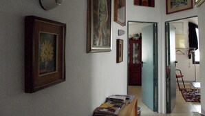 A hallway with framed artwork on the walls, a wooden cabinet, and a table with books. - B&B L'Intrigante (Seborga)
