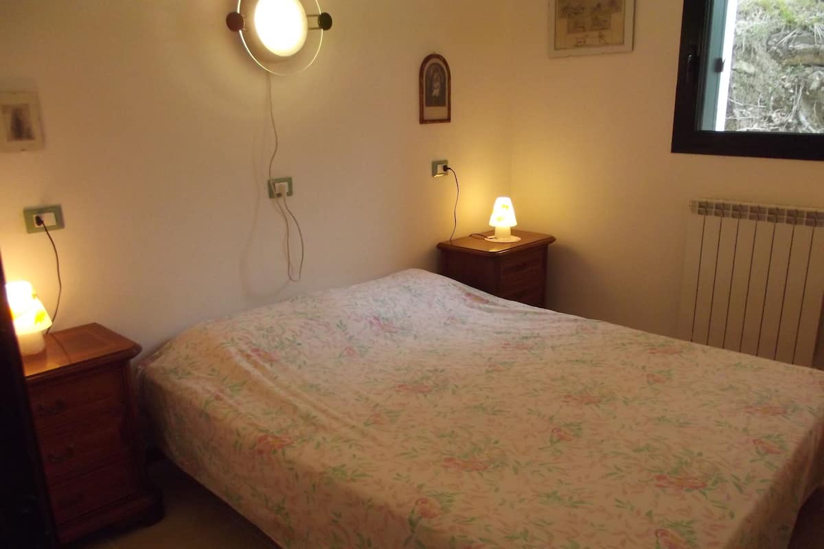 A bedroom with a bed, two bedside tables with lamps, a wall socket, and a radiator.
