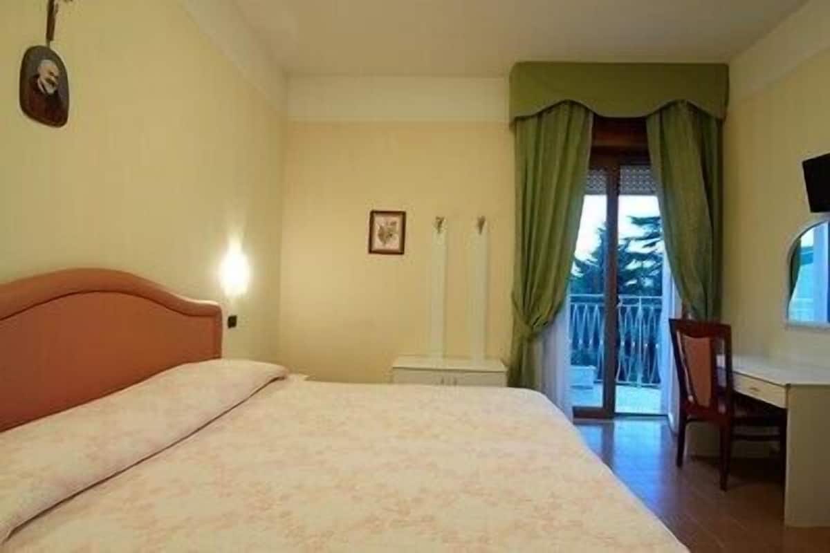 Un dormitorio con cama, un escritorio y una silla. Hay una ventana con cortinas.