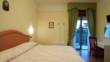 A bedroom with a bed, a desk, and a chair. There is a window with curtains.