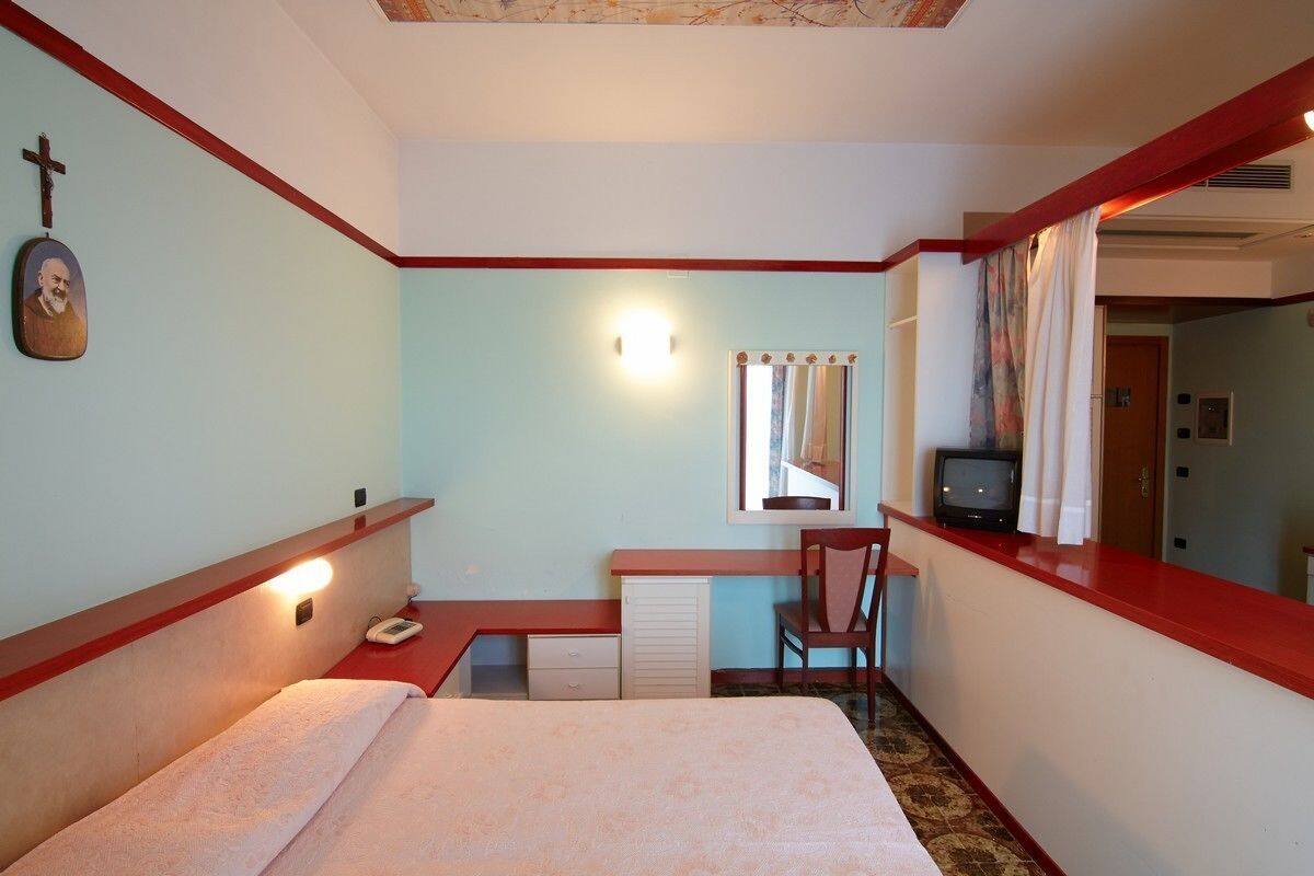 Una habitación pequeña y acogedora con una cama, un escritorio, una silla, un televisor y un espejo.