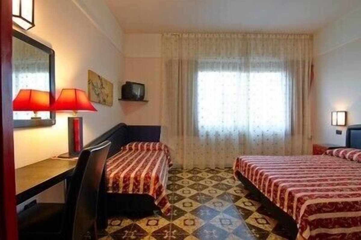 Habitaci ón de hotel con dos camas, un escritorio, una silla, una lámpara y una ventana con cortinas.