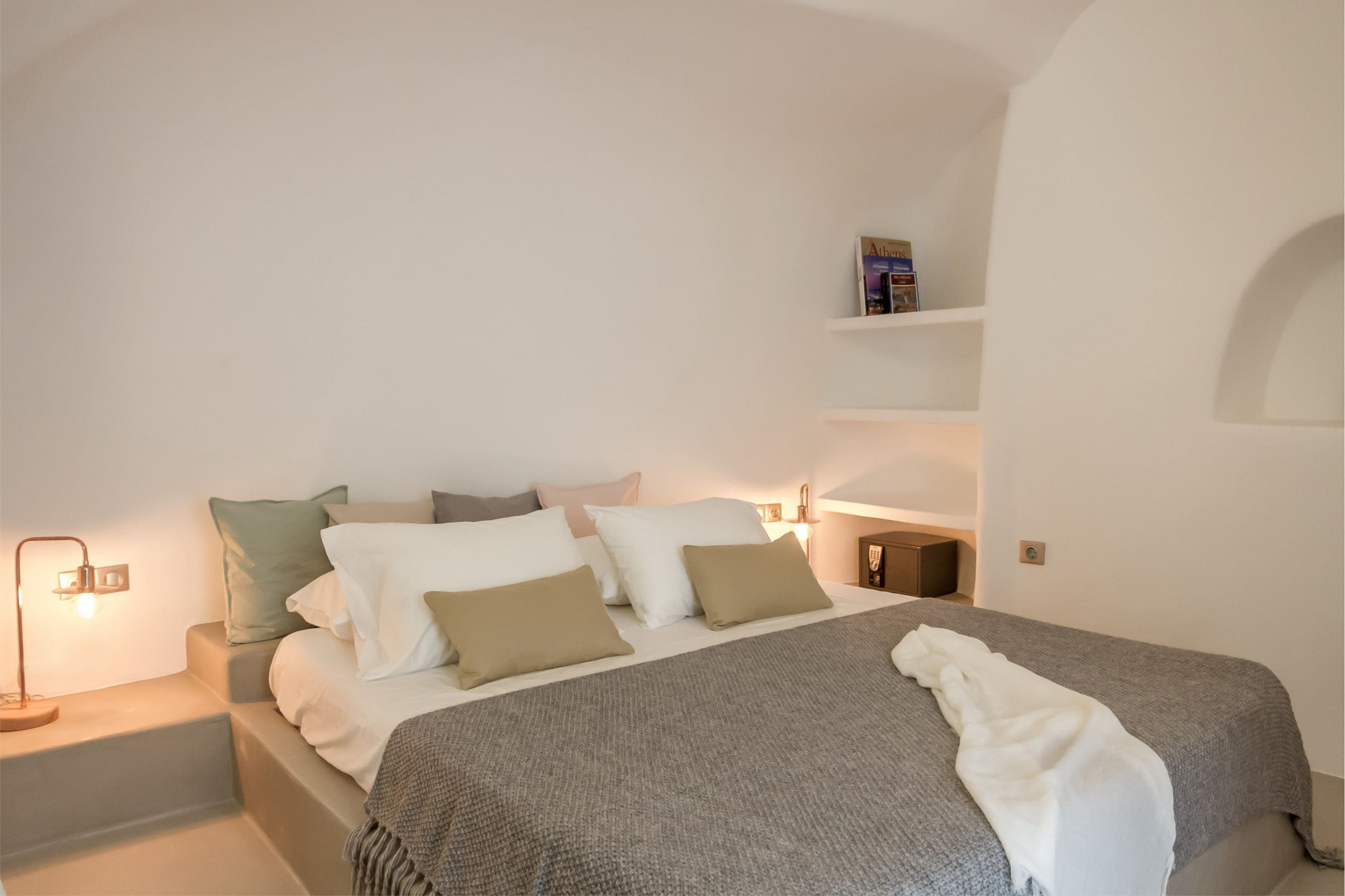 A neatly arranged bedroom with a bed, pillows, a bedside table, and a shelf with a book.