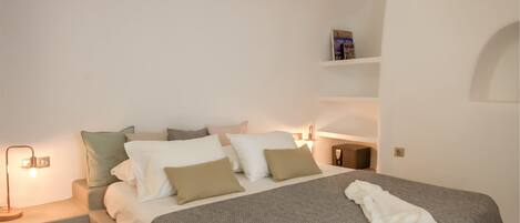 A neatly arranged bedroom with a bed, pillows, a bedside table, and a shelf with a book.