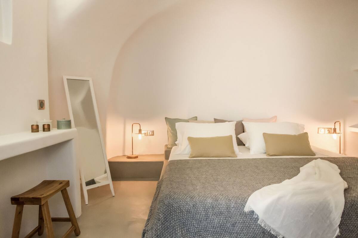 A bedroom with a bed, bedside tables, a mirror, and a small stool.