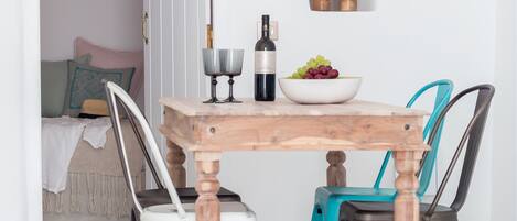 A dining area with a wooden table, four chairs, a bowl of fruit, a wine bottle, and a geometric pendant light.