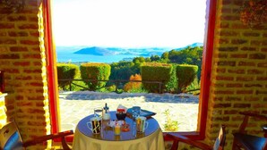 A table set with drinks and a menu, overlooking a beach and mountains. - Loggas Hotel (Kastoria)