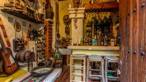 A narrow, cluttered room with shelves filled with various bottles, a guitar, and a rustic wooden door. - La Casona Albaida (Albaida)