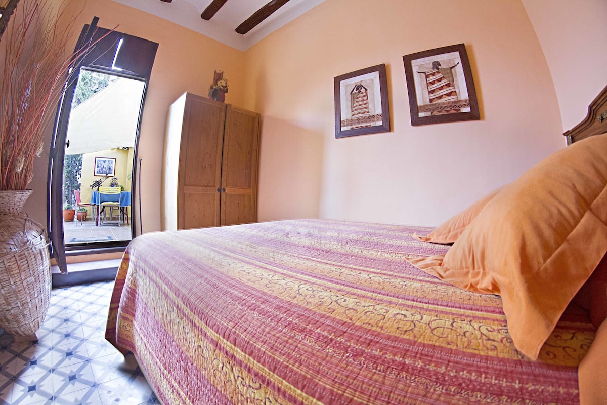 A bedroom with a bed, a wooden wardrobe, and two framed pictures on the wall.