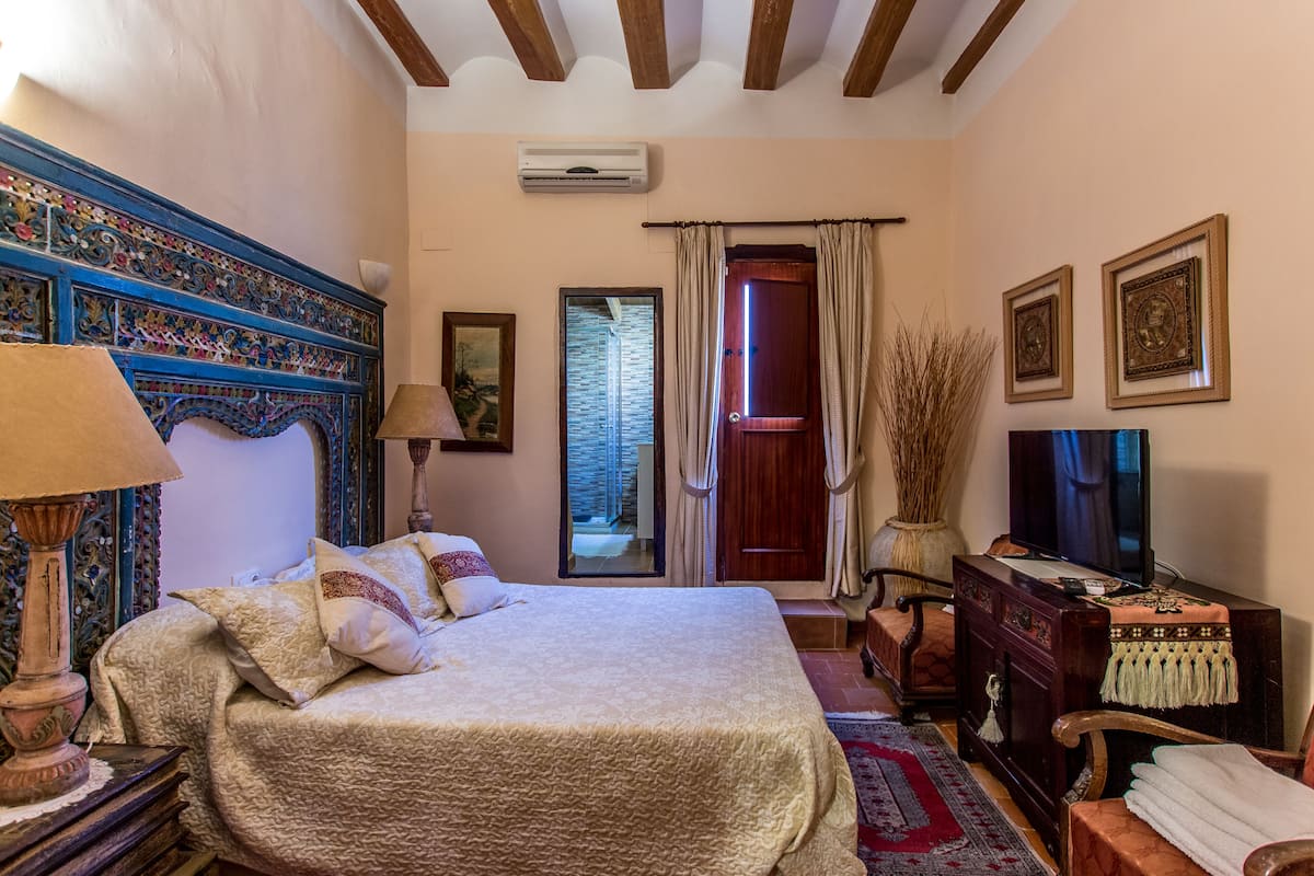 A bedroom with a bed, a dresser, a television, and a window with curtains.