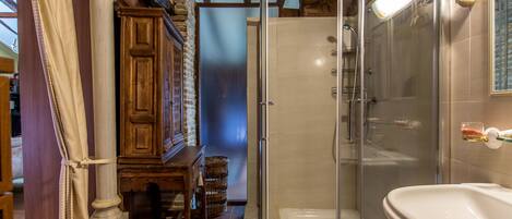 Un baño con ducha acristalada, lavabo blanco y muebles de madera.