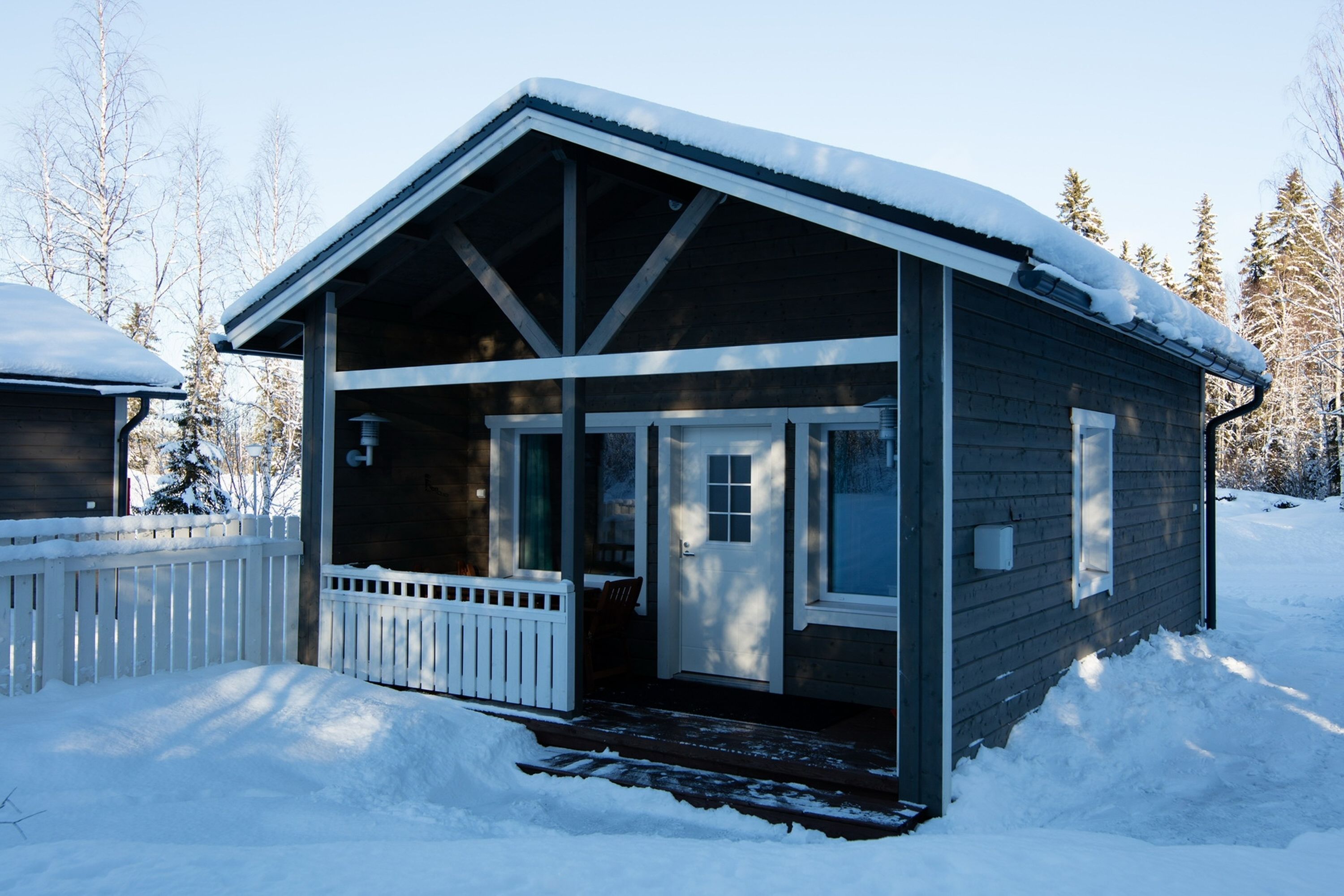 Eine Holzhütte mit Veranda und schneebedecktem Dach, umgeben von Bäumen.