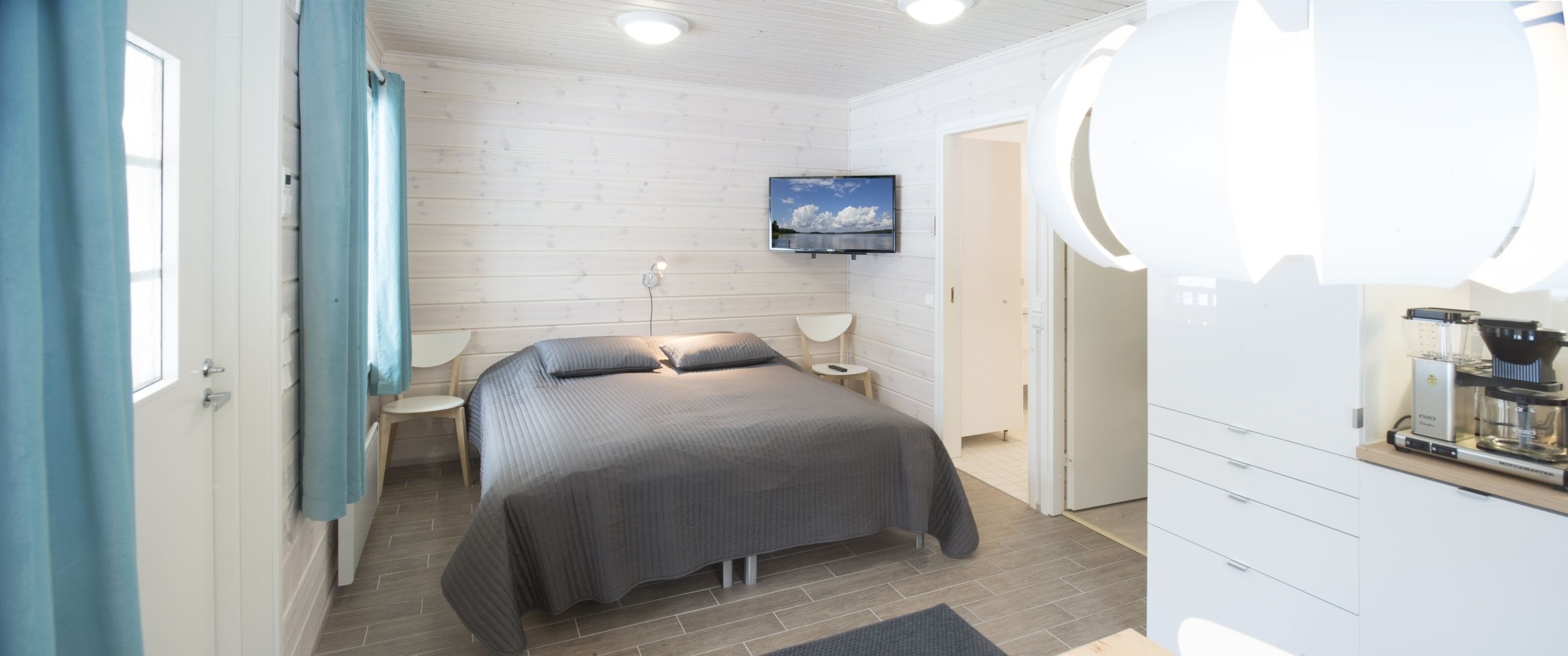 Une chambre moderne équipée d’un lit, de tables de chevet, d’un téléviseur et d’une machine à café.