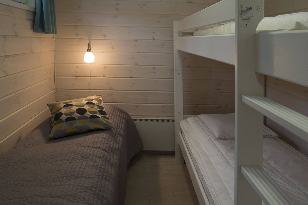 Ein kleines, gemütliches Zimmer mit einem Einzelbett, einem Kopfkissen und einer Wandleuchte.
