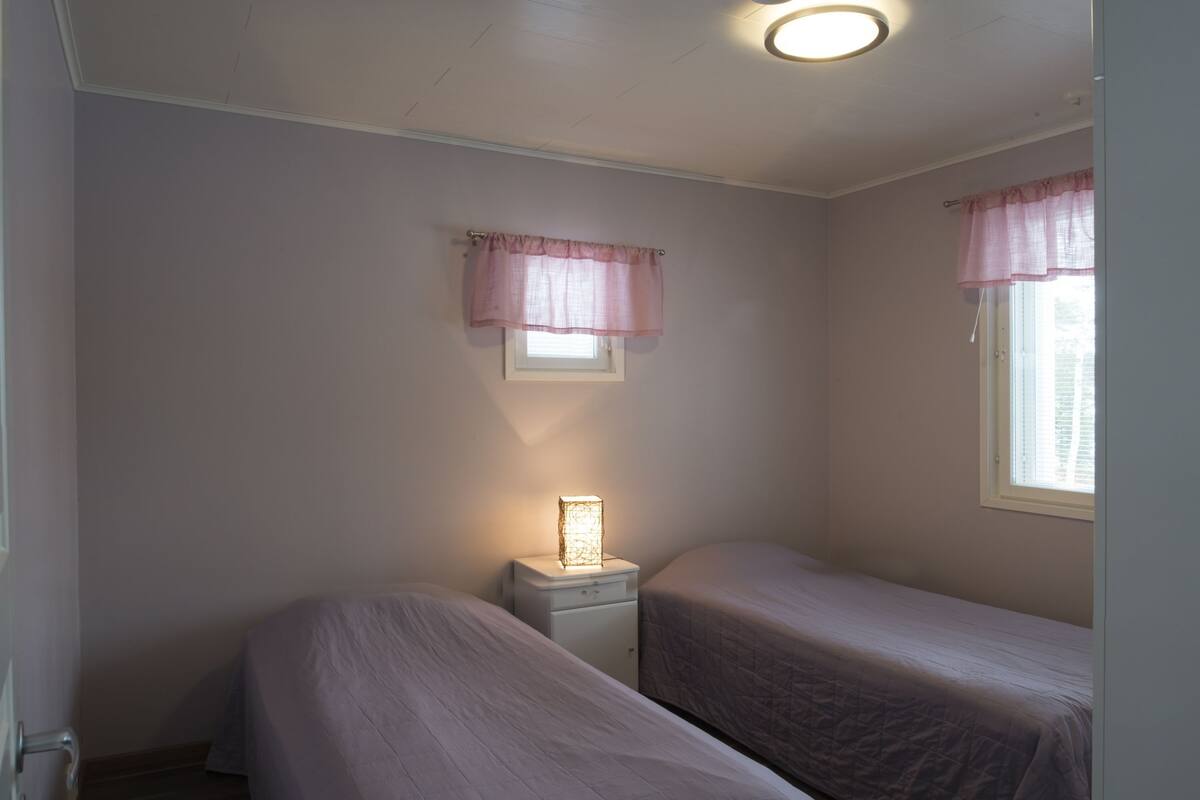 Ein kleines Schlafzimmer mit zwei Einzelbetten, einem Nachttisch mit Lampe und einem Fenster mit Vorhang.