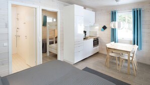 Una habitación moderna con cama, una kitchenette pequeña, un área de comedor con mesa y sillas, y una ventana con cortinas.