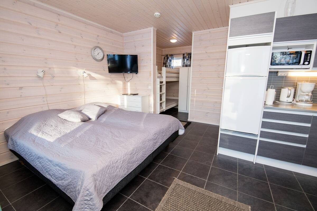 Ein Schlafzimmer mit Bett, Fernseher, integriertem Kleiderschrank und einer Küchenzeile inklusive Mikrowelle und Kaffeemaschine.