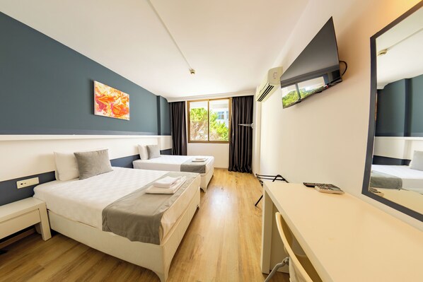 Una habitación de hotel con dos camas, un escritorio, un televisor y una ventana con cortinas.