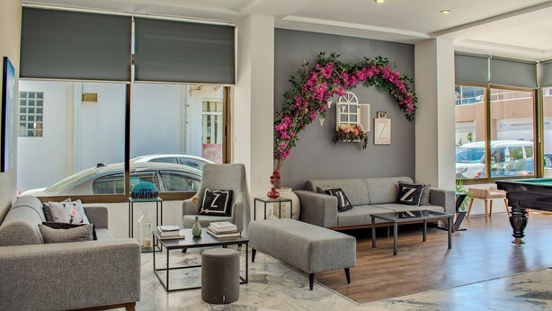 A spacious living area with a grey sofa set, a coffee table, and a decorative arch with pink flowers. - Z Otel (Cesme)