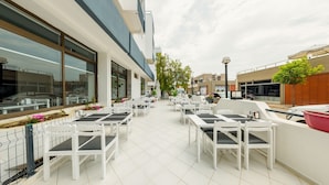 An outdoor patio area with white tables and chairs, a tiled floor, and a view of the street. - Z Otel (Cesme)
