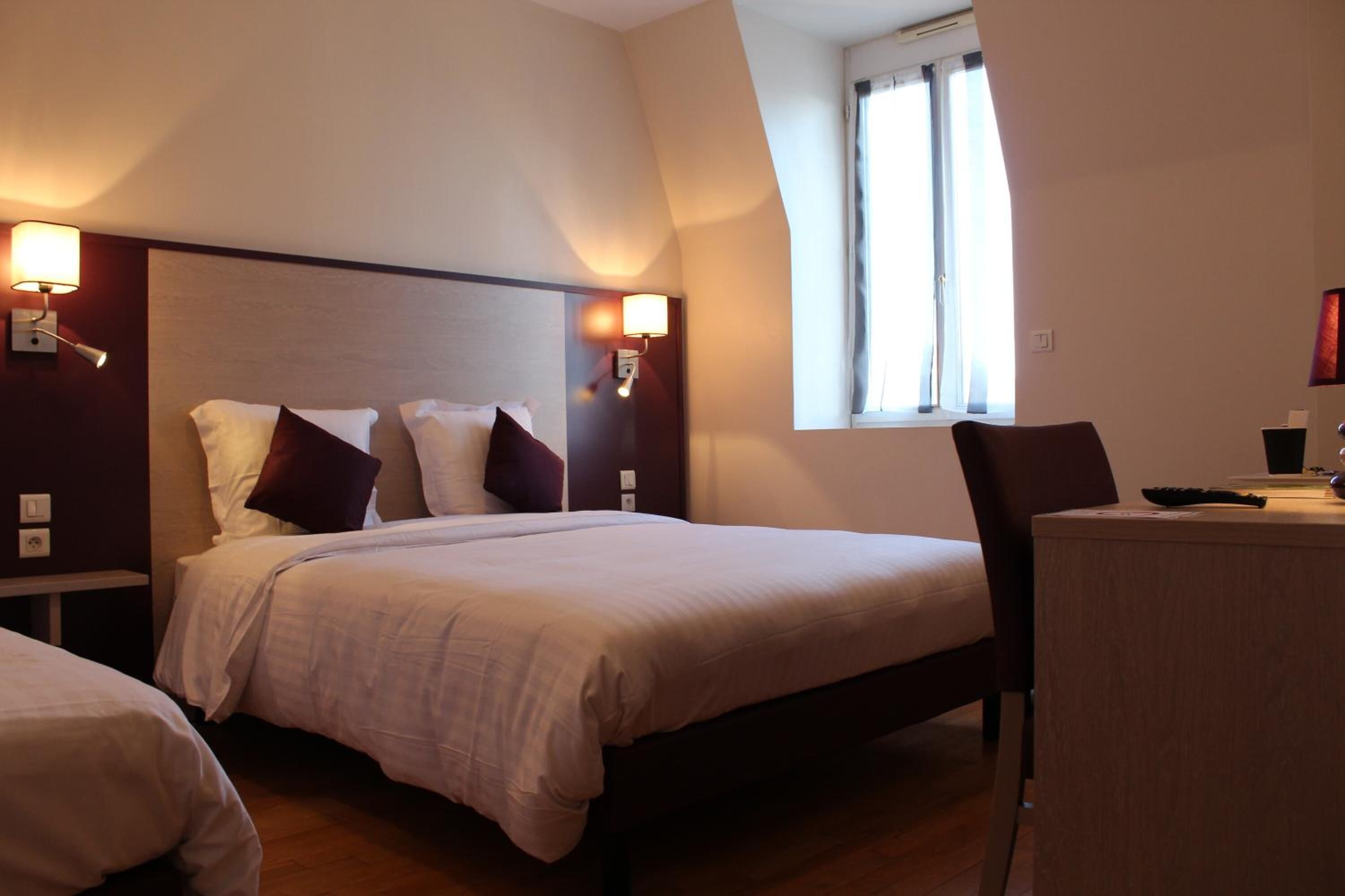 Quarto de hotel com uma cama grande, duas mesas de cabeceira, uma escrivaninha com cadeira e uma janela com cortinas.