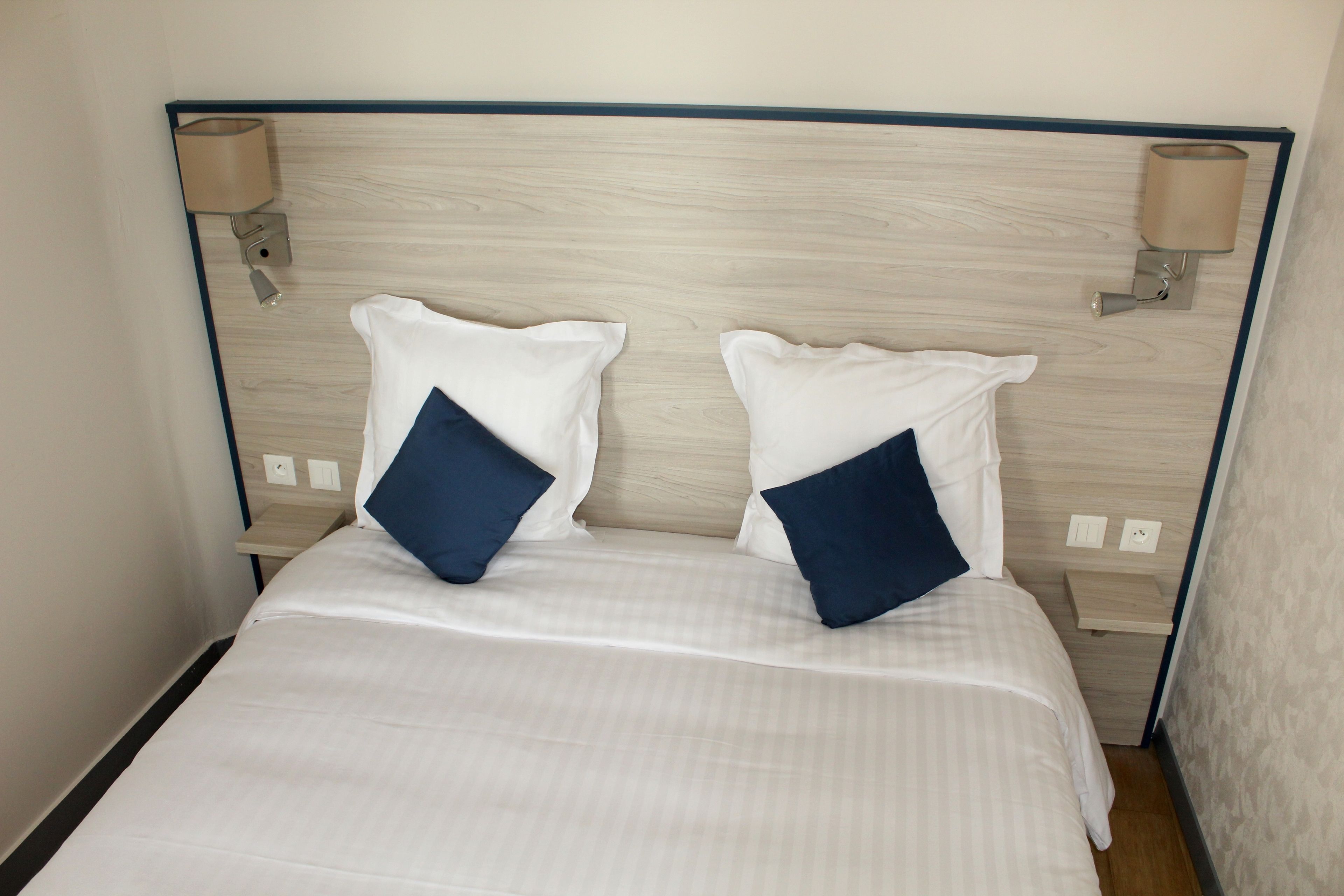 Habitación de hotel con cama, dos almohadas, mesita de noche y lámparas de pared.