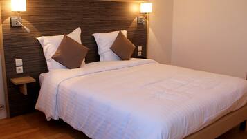 A neatly made bed with white linens and two brown pillows, a wooden headboard, and two wall-mounted lamps.