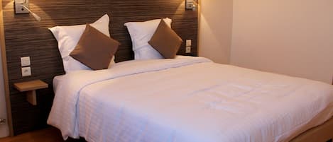 A neatly made bed with white linens and two brown pillows, a wooden headboard, and two wall-mounted lamps.