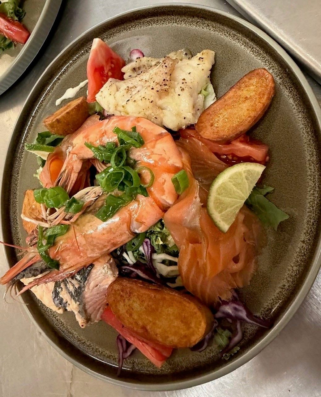 Un plato de mariscos que incluye camarones, salmón y un trozo de pescado, acompañado de una rodaja de limón y una guarnición de cebollines.
