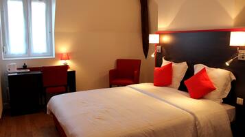 A hotel room with a bed, a desk, a chair, and two bedside lamps.