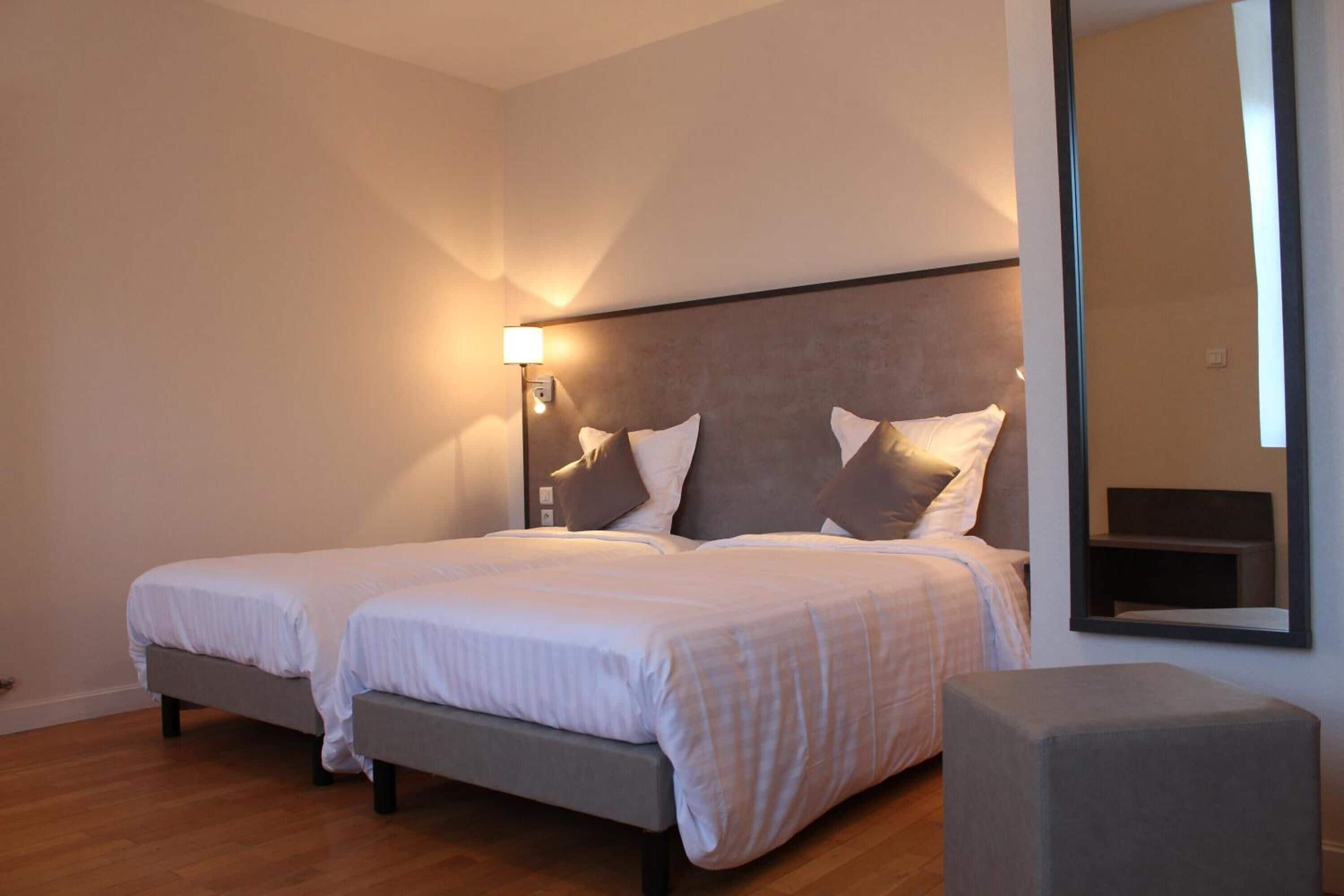A double bed with two pillows, a bedside table, and a nightstand in a hotel room.