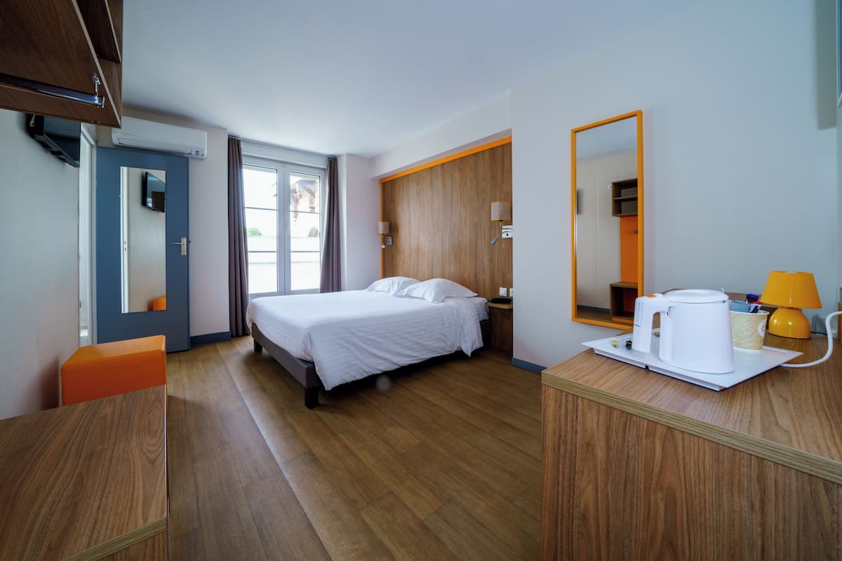 Ein Hotelzimmer mit Bett, Schreibtisch, Stuhl, Kaffeemaschine, Lampe und Spiegel.