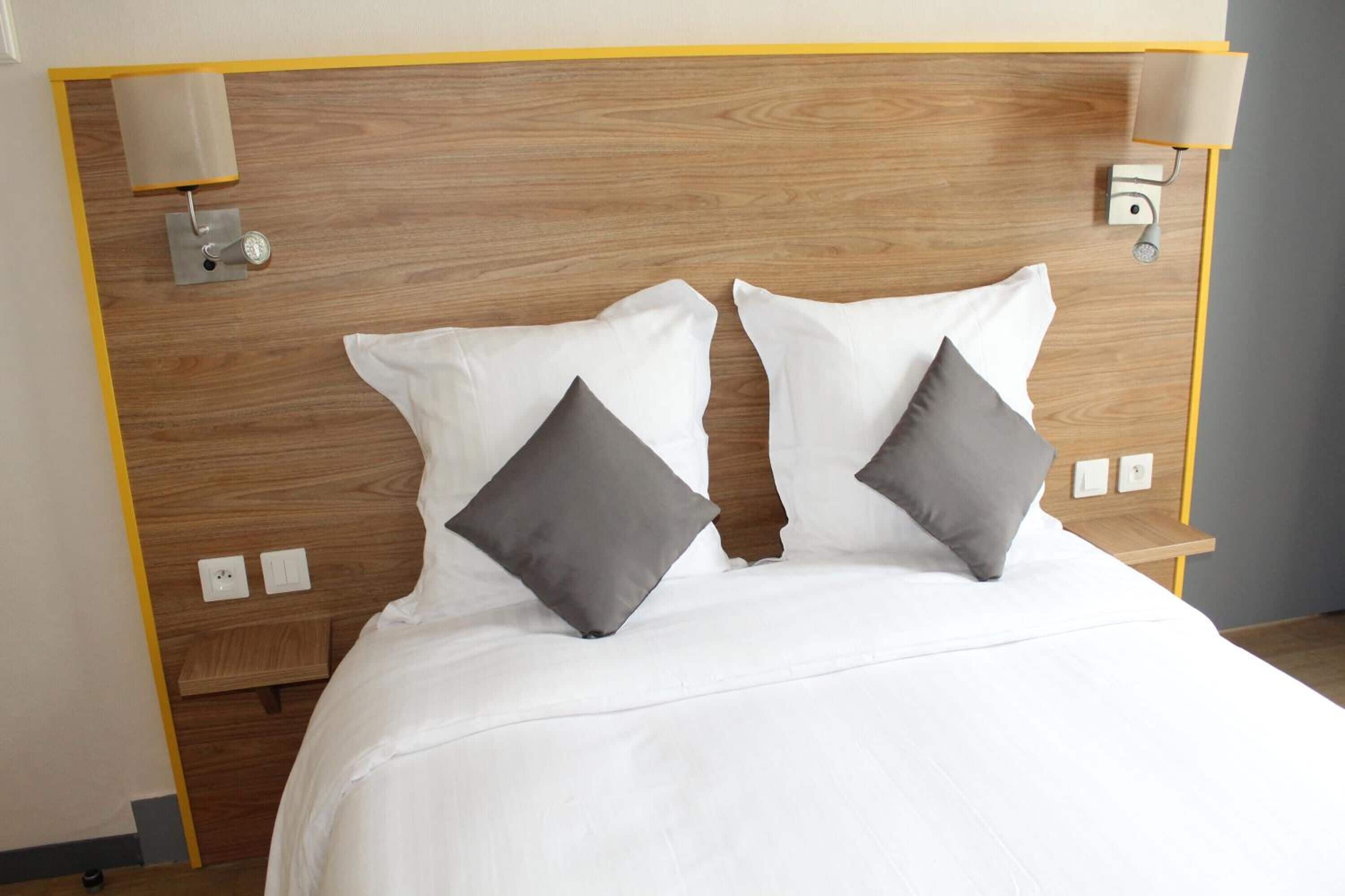 A neatly made bed with white bedding and two gray pillows, a wooden headboard, and bedside lamps.
