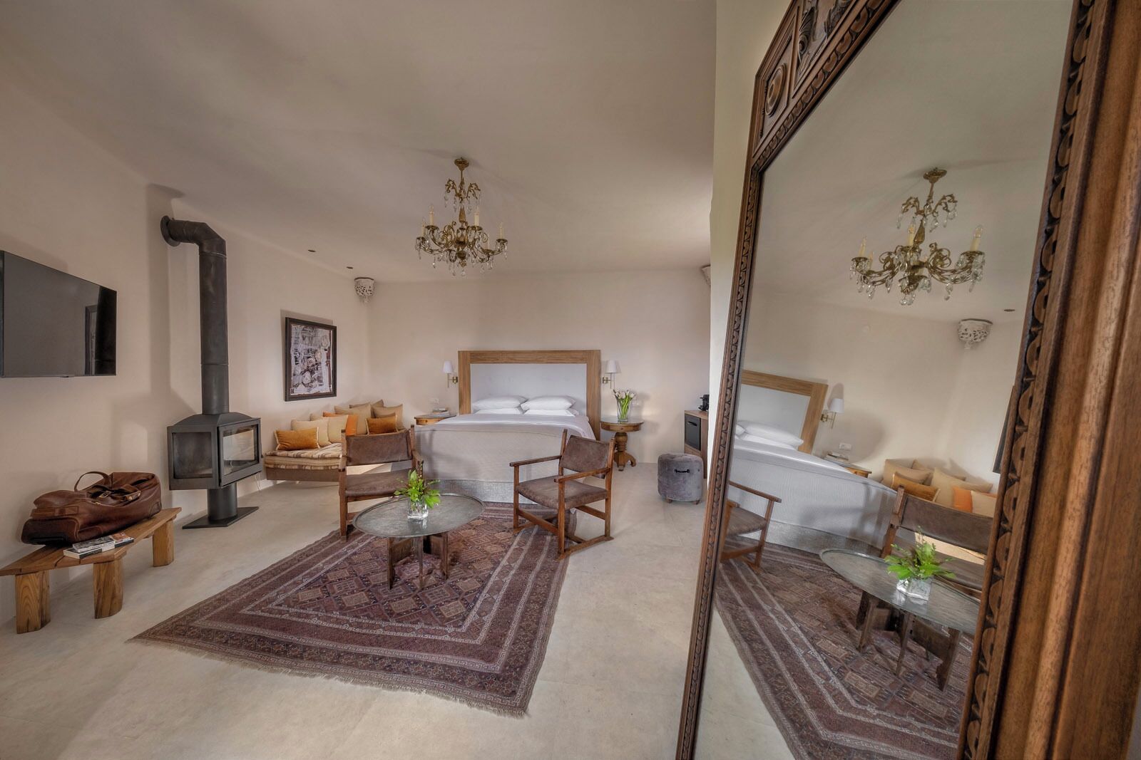 A modern hotel room with a large bed, a sofa, a small table, a TV, and a fireplace.
