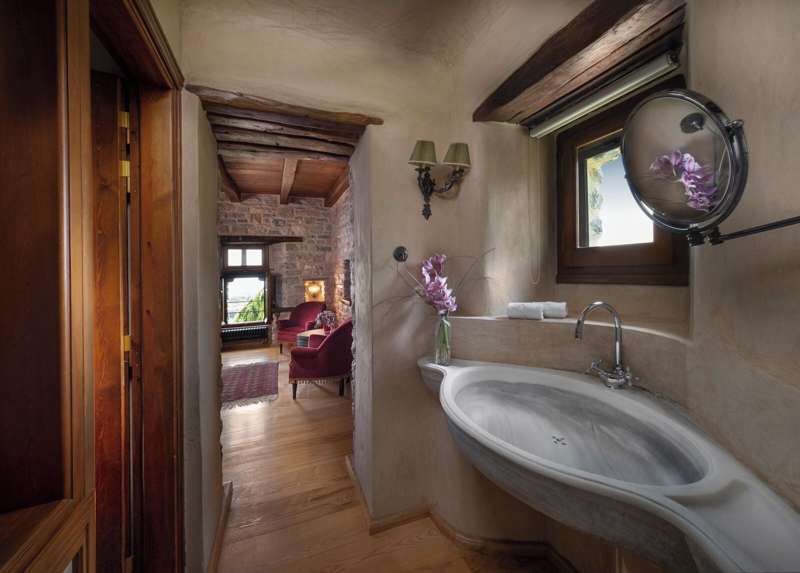 Un baño con pared de piedra, techo de madera, un lavamanos grande y una ventana con espejo.
