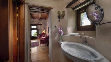 Un baño con pared de piedra, techo de madera, un lavamanos grande y una ventana con espejo.