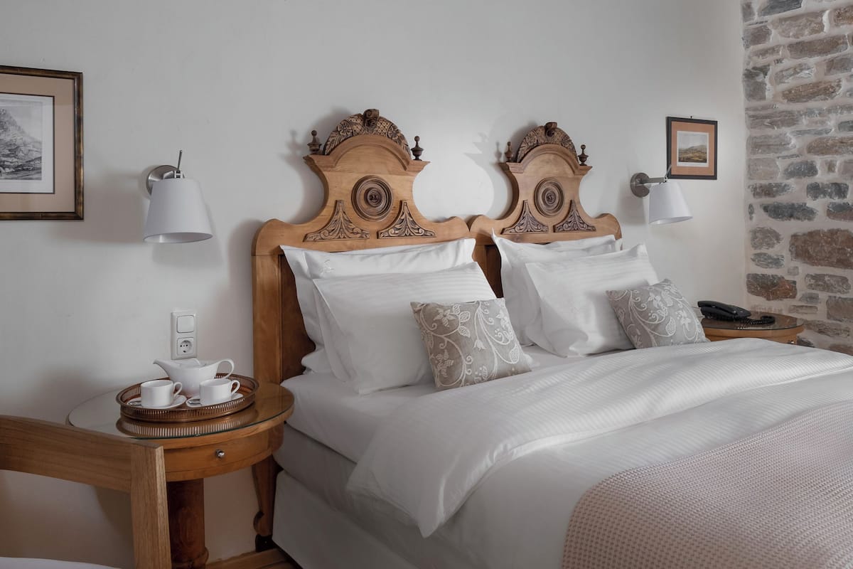 A bedroom with a wooden ceiling, a stone wall, and a bed with white bedding.