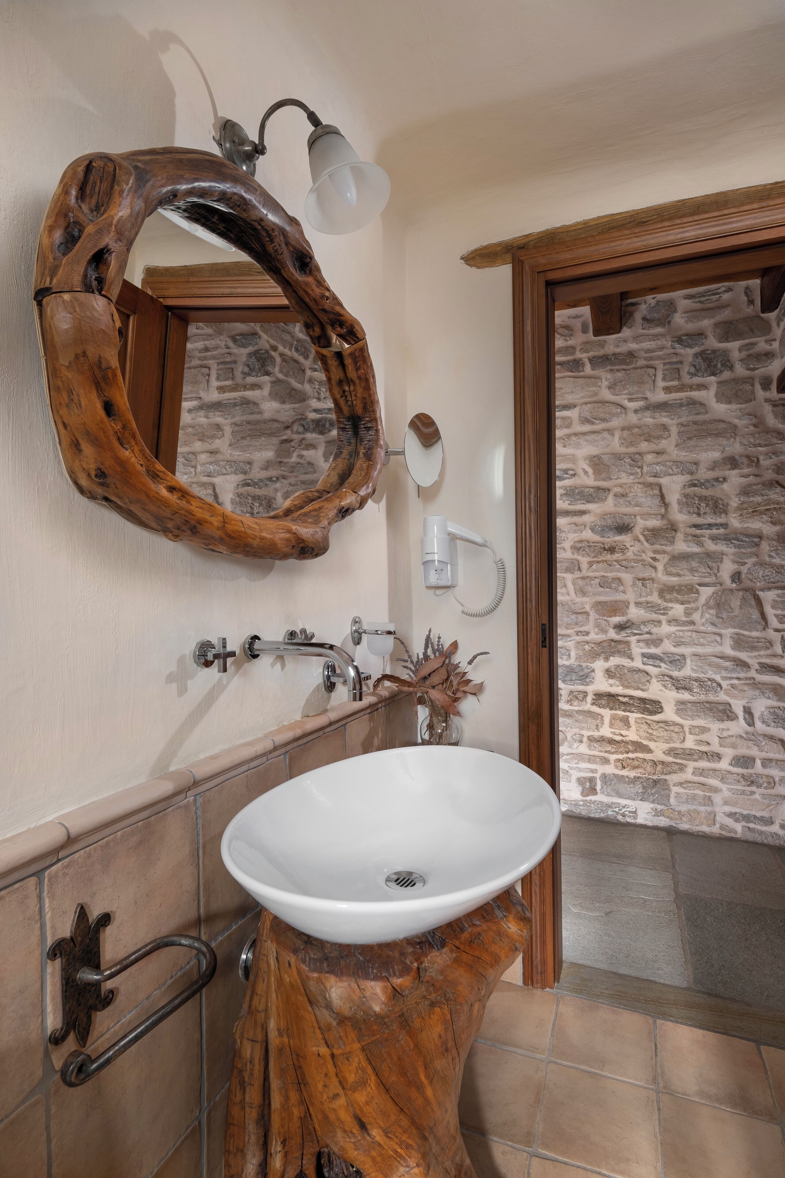 A bathroom with a wooden vanity, a white sink, a stone wall, and a mirror with a wooden frame.