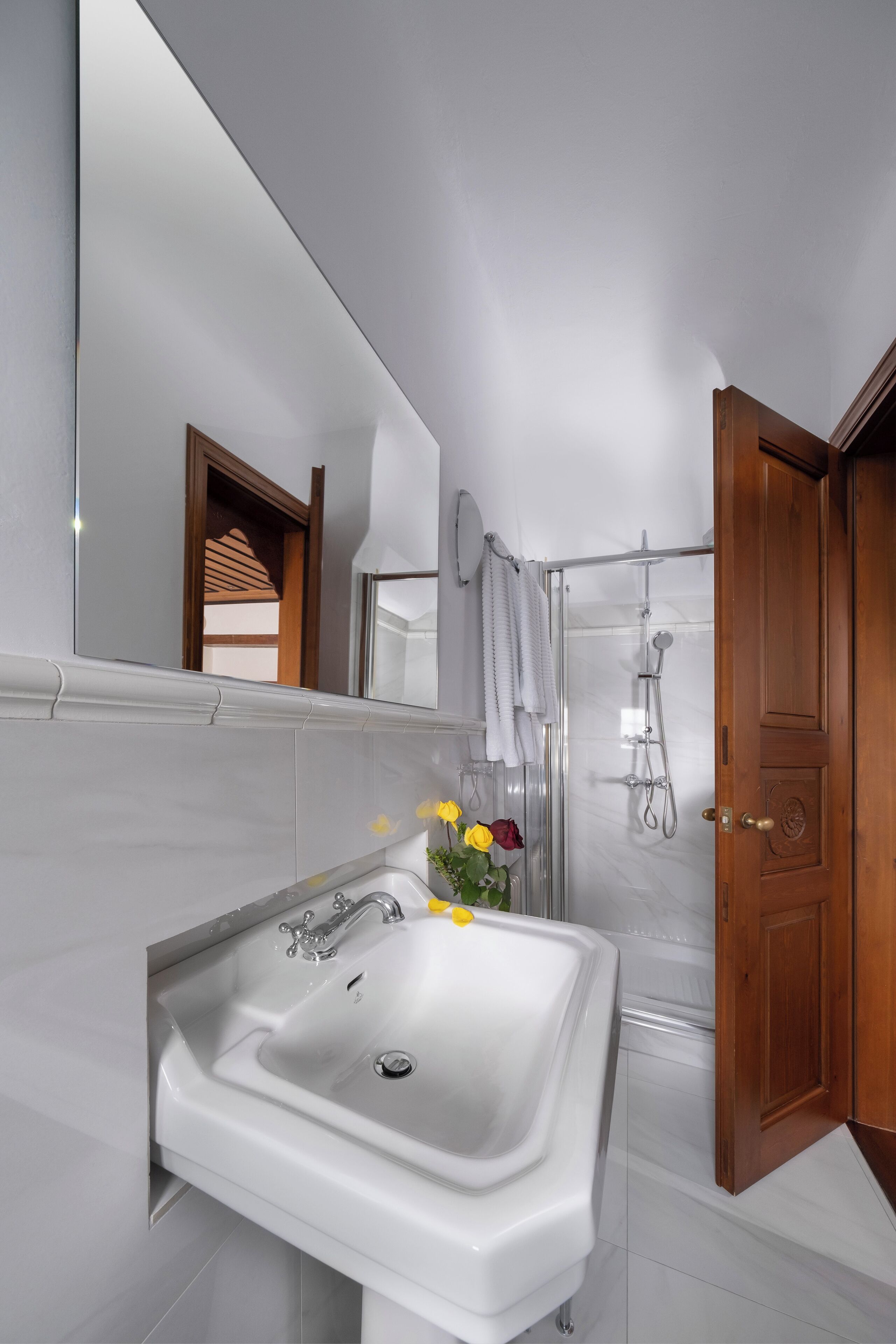 Un baño moderno con un lavamanos blanco, cabina de ducha con mampara de vidrio y una puerta de madera.