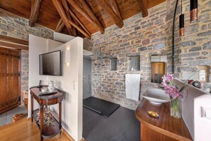 Un baño rústico con pared de piedra, vigas de madera, un lavamanos, un espejo y una ducha.