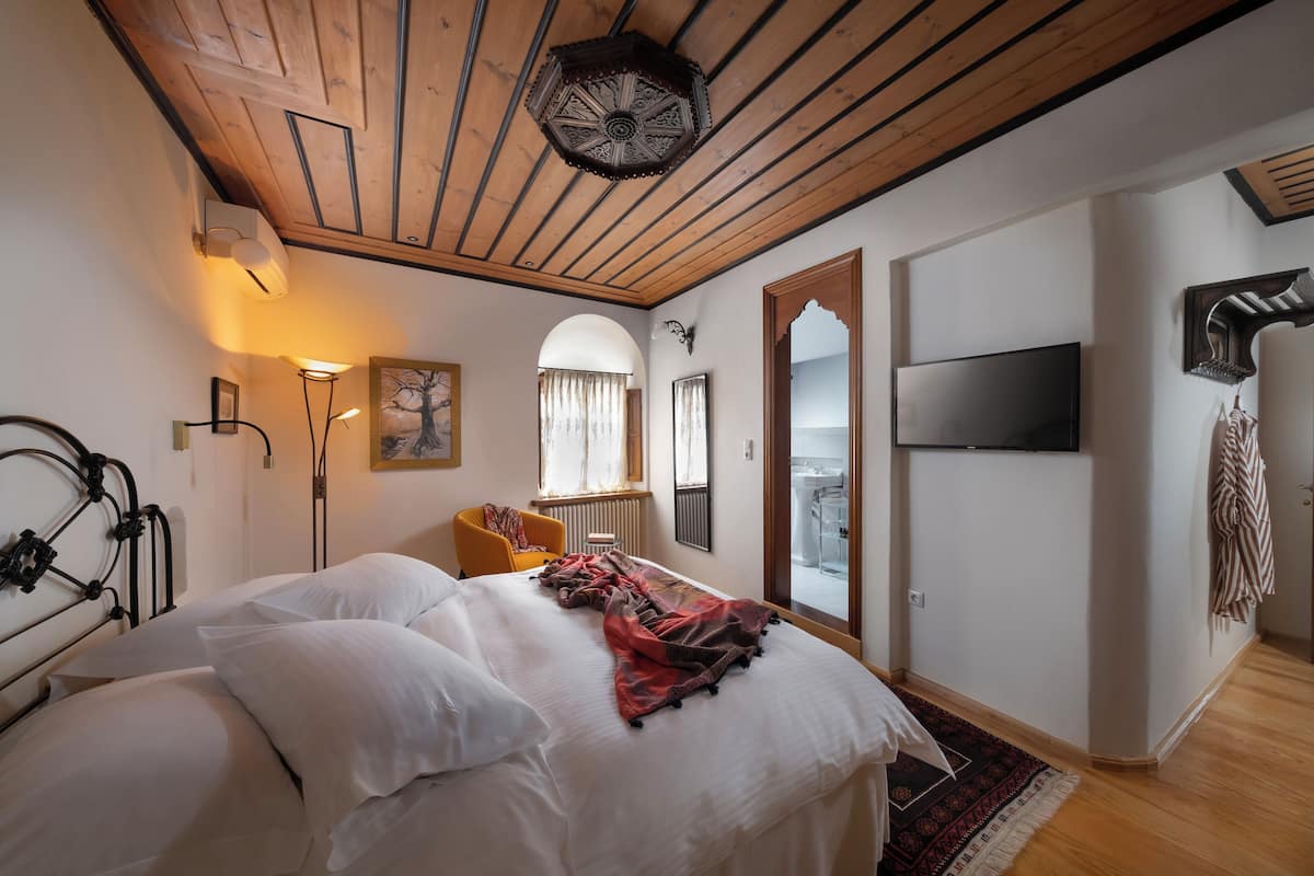 A bedroom with a bed, a chair, a TV, and a view of the outside.