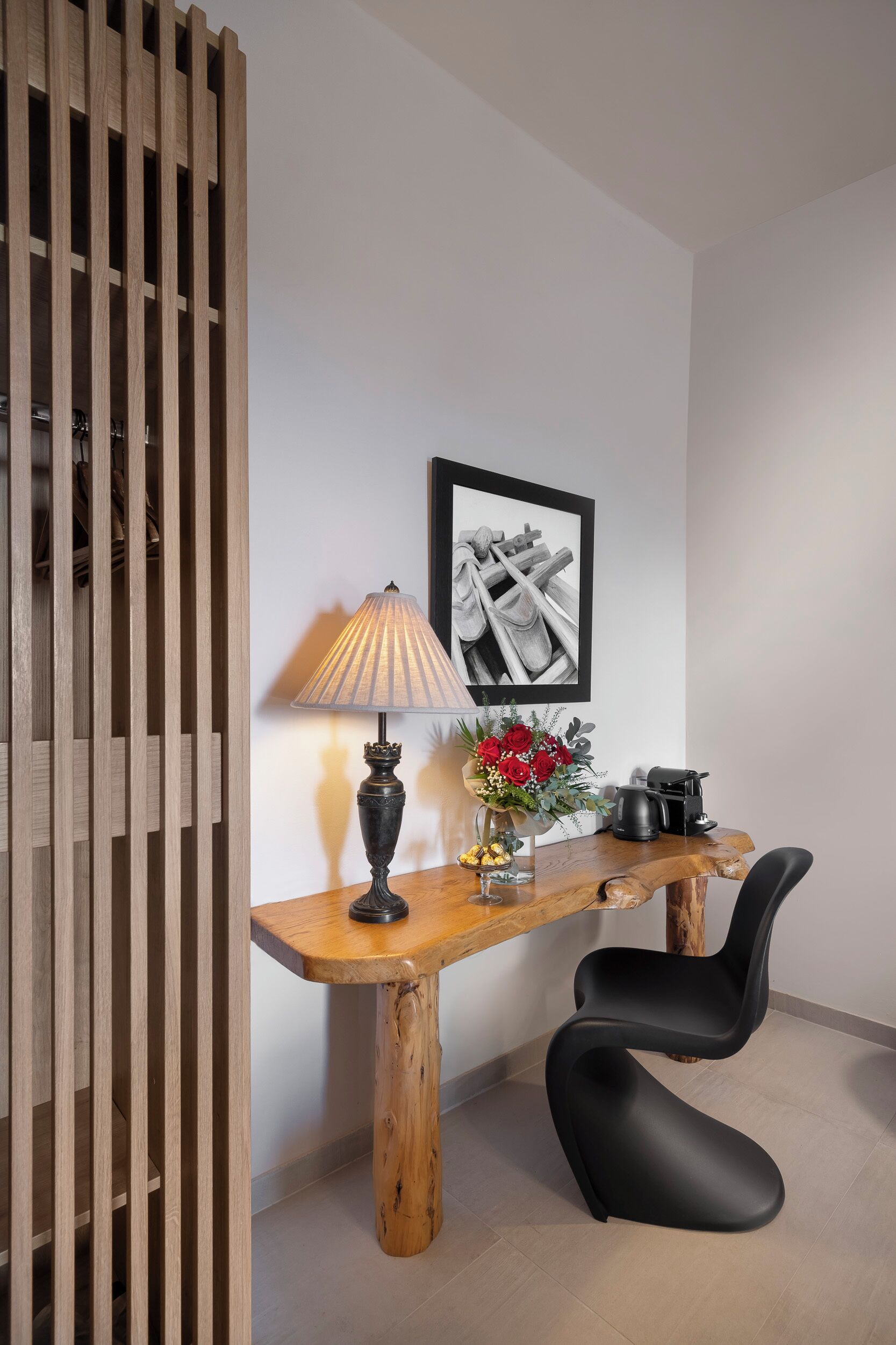 A wooden table with a lamp, a vase with flowers, and a framed picture on the wall.