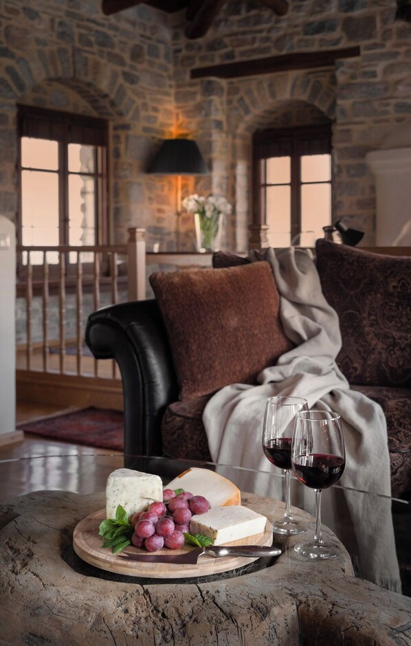A stone-walled room with a leather sofa, a wooden table with cheese, grapes, and wine glasses. - Sakali Mansion (South Pelion)
