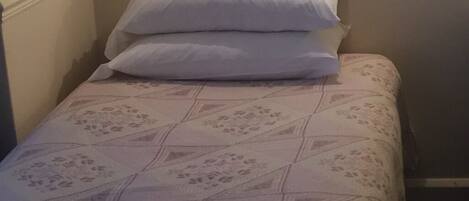 Ein kleines Zimmer mit einem Einzelbett, einer floralen Tagesdecke und zwei Kissen.