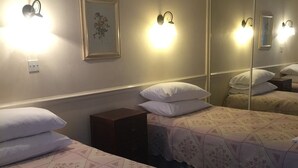 A hotel room with two beds, each with a floral-patterned bedspread and white pillows. There are wall-mounted light fixtures and a framed picture on the wall. - Colnbrook Lodge Guest House (Slough)