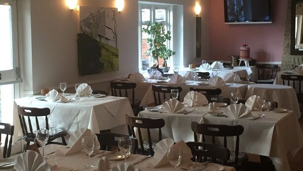 A dining area with multiple tables set for service, a large painting on the wall, and a television mounted on the wall. - Colnbrook Lodge Guest House (Slough)