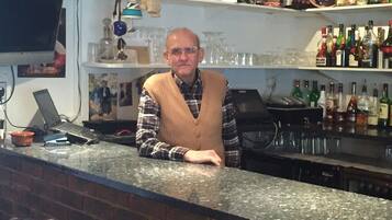 Una zona de bar con mostrador, estantes con botellas, vasos y un televisor montado en la pared.