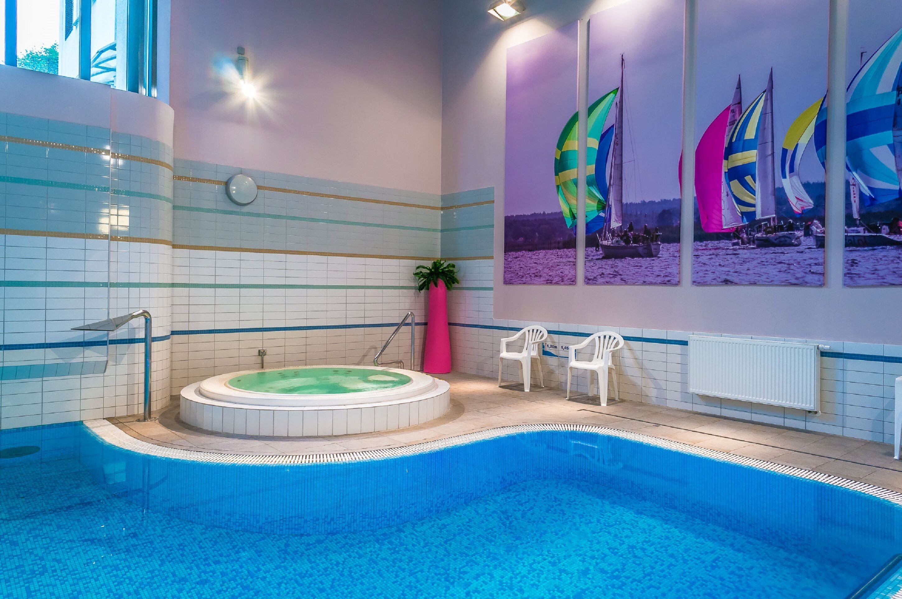 A swimming pool with a hot tub, tiled walls, and a mural of sailboats.
